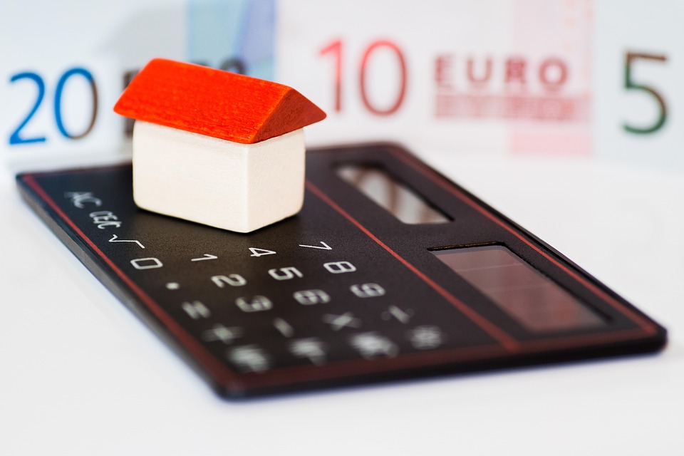 Calculator, model house, coins, and euro banknotes used for budgeting
